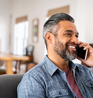 Man in blue collared shirt smiling while talking on phone